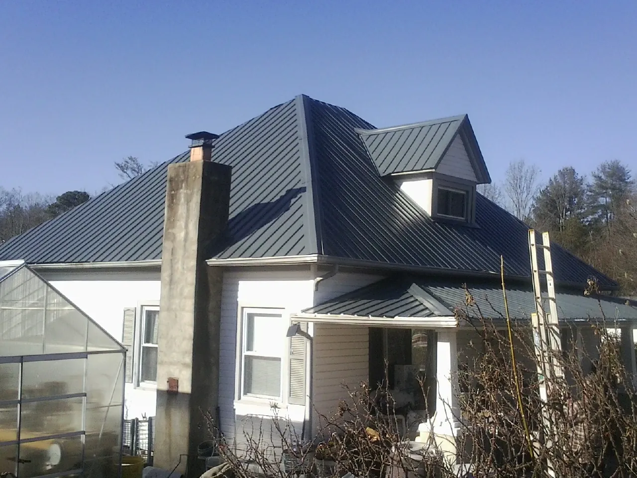 Dark blue standing seam metal roof on a white farmhouse with dormer — Slate & Tile Roof Repair by Roofing Brothers in Happy Jack