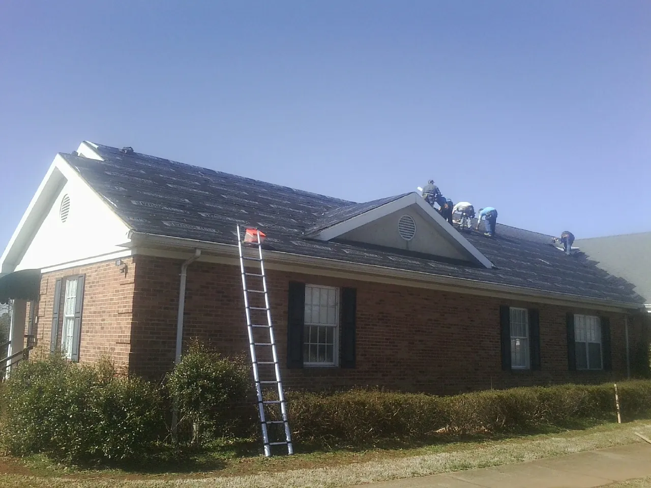 Crew tearing shingles off a brick ranch roof with a ladder set — Metal Roof Repair work by our crew in Happy Jack