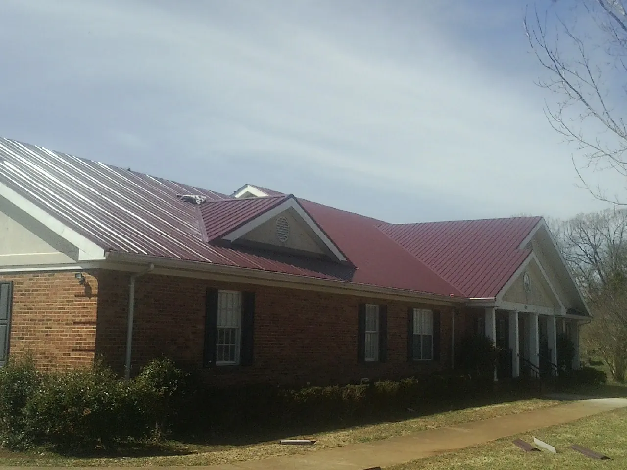 Red metal roof with gabled entries on a long brick building, from a Hail Damage Roof Repair job in Happy Jack
