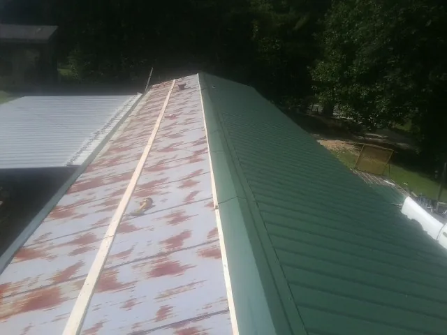 Old rusted panels beside newly installed green metal roofing — Wind Damage Roof Repair by Roofing Brothers in Happy Jack