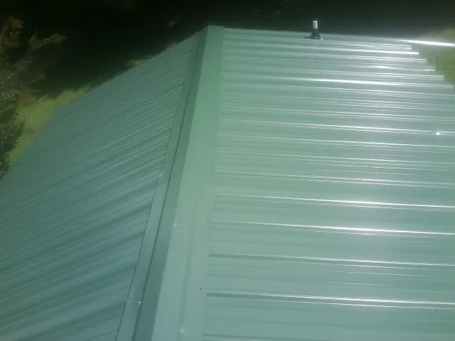 New green metal panels meeting at the ridge of a roof — Flat Roof Repair work by our crew in Happy Jack