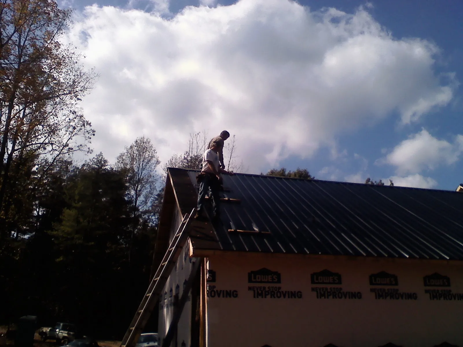 Roofer fastening dark metal panels high against a cloudy sky, from a Roof Inspection job in Happy Jack