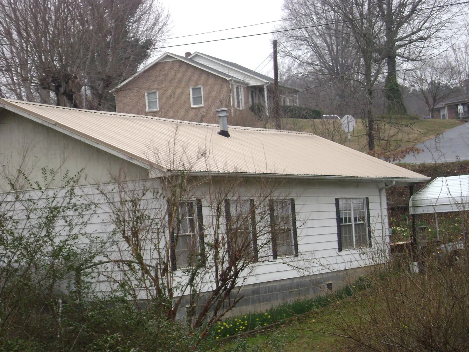 Tan metal roof on a white sided house set into a hillside — Commercial Roofing by Roofing Brothers in Happy Jack